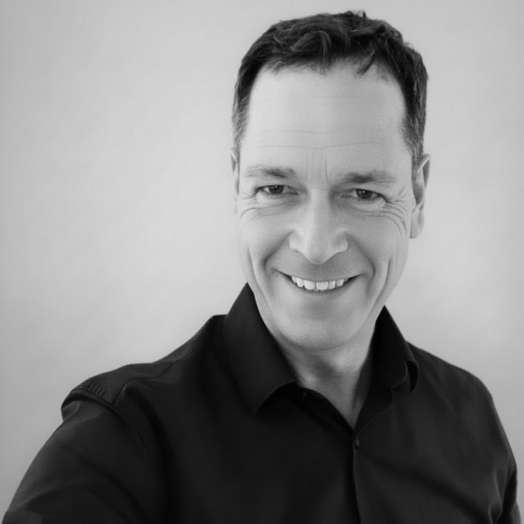 Schwarzweißfoto eines Mannes in Hemd, der lächelnd in die Kamera schaut